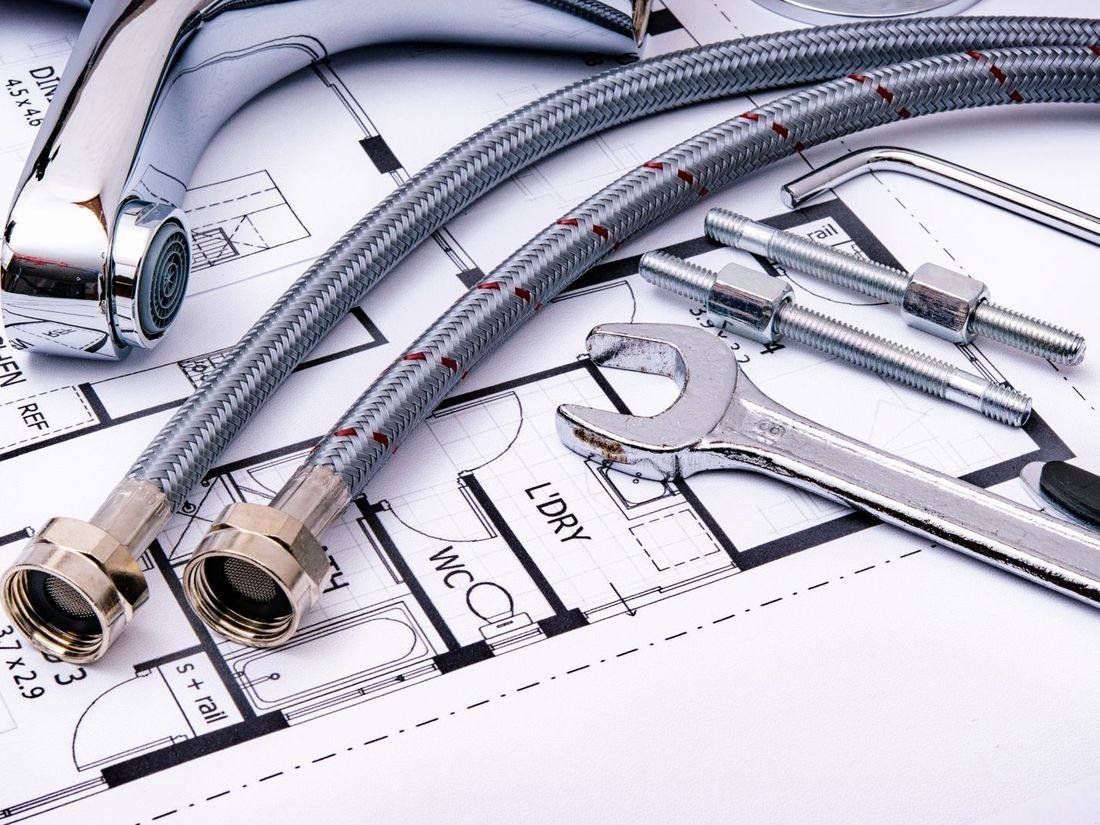 Plumbing fittings, hoses and a wrench laid out on a plan