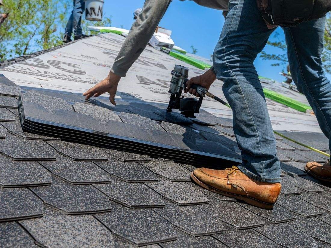 Roofer fastening new shingles with a nail gun
